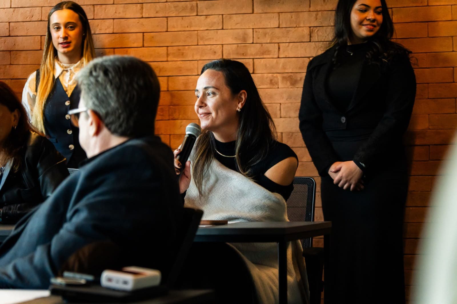 Liane Almeida falando ao microfone em um evento para donos de assistência técnica
